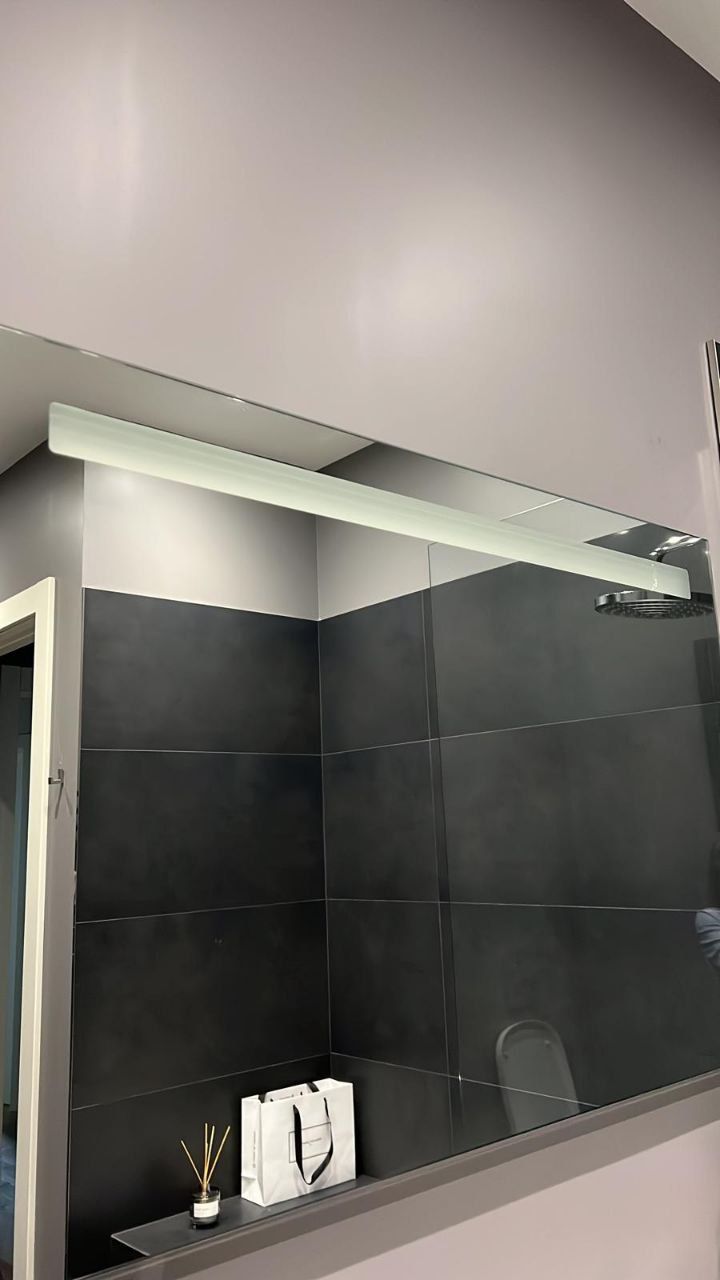 Modern bathroom with a sleek glass shower partition and dark grey tiled walls.