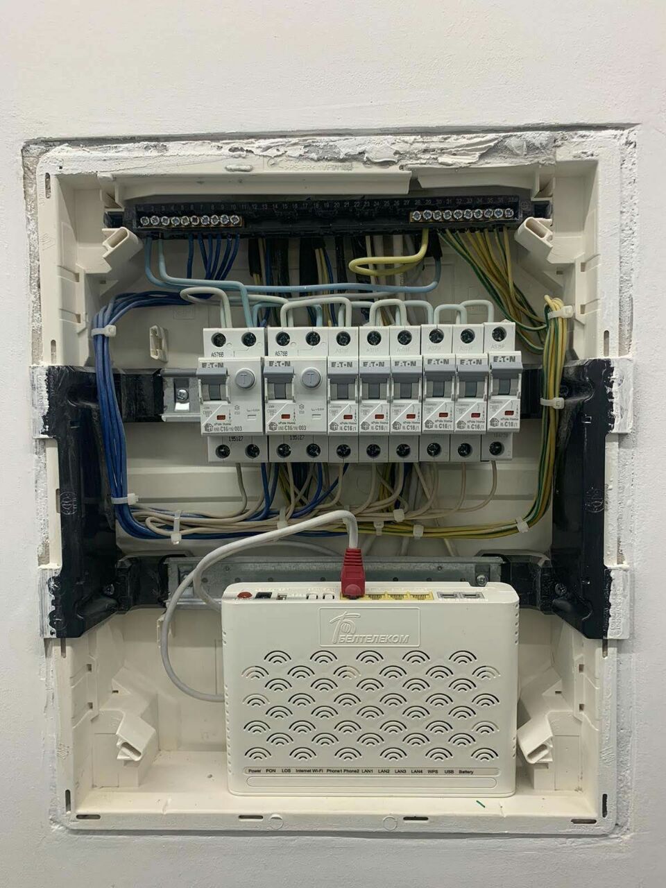 Open white electrical panel with multiple circuit breakers and a white modem device.