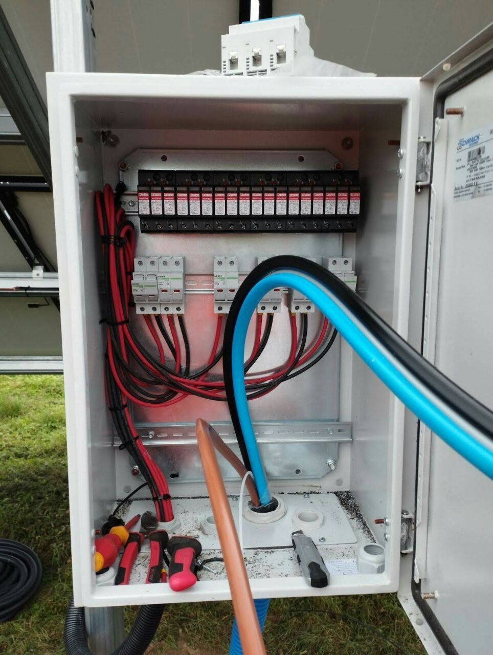 Open electrical control box displaying red and black wiring connected to terminal blocks with tools.