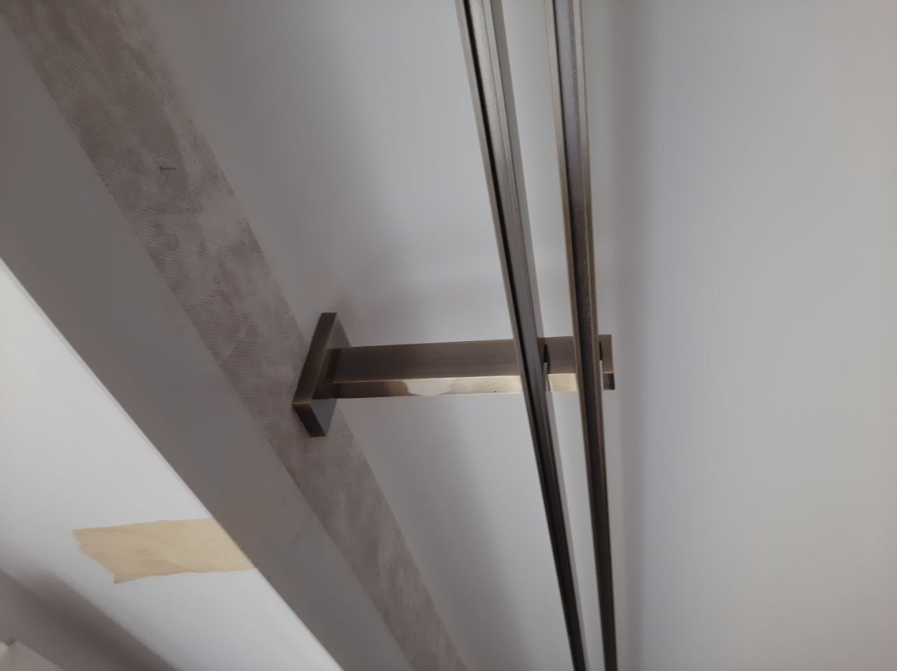 A modern double curtain rod bracket secures two metal rods to a white wall.