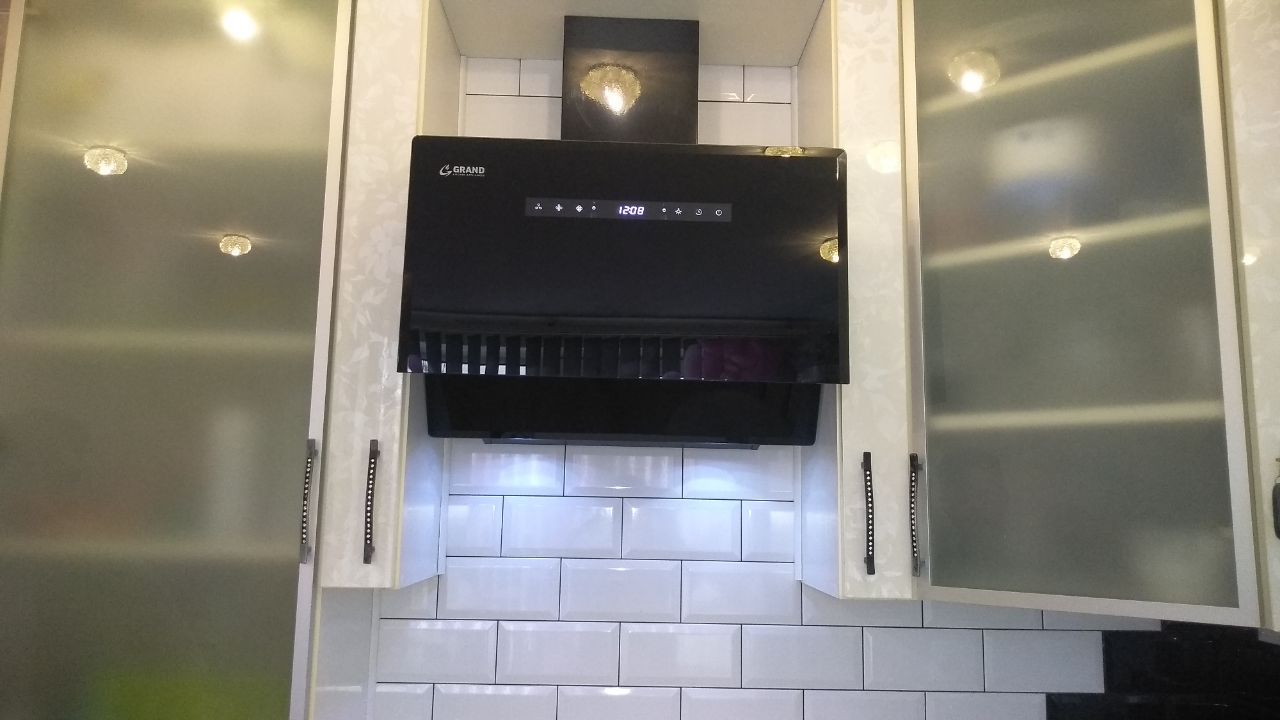 A modern black kitchen hood installed between white cabinets above a white tiled backsplash.