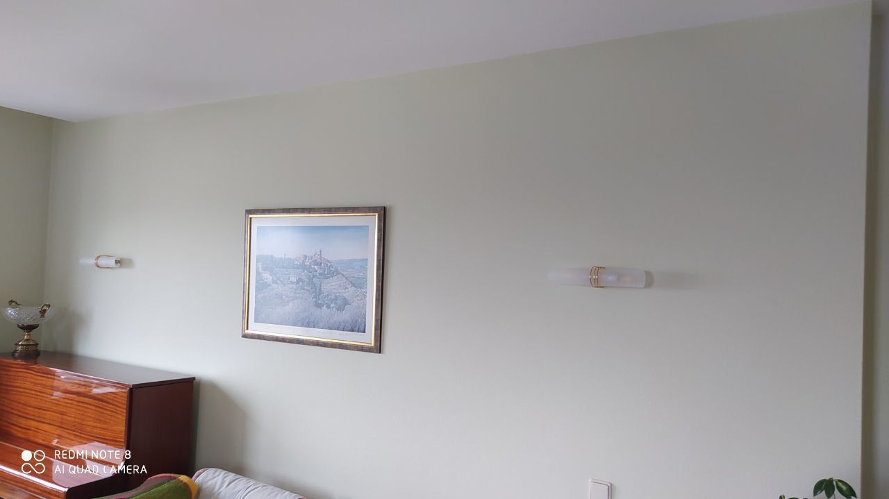 Light green wall featuring a framed landscape picture, wooden dresser, and two wall lights.