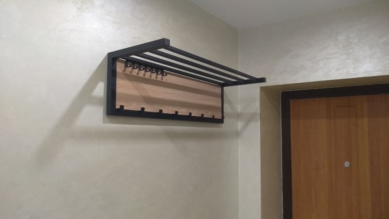 Modern wall-mounted coat rack with a dark metal frame and light wood panels.