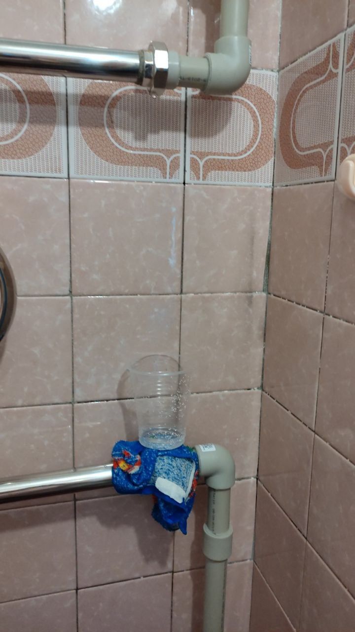 A blue and white water filter connected to pipes on a tiled bathroom wall.