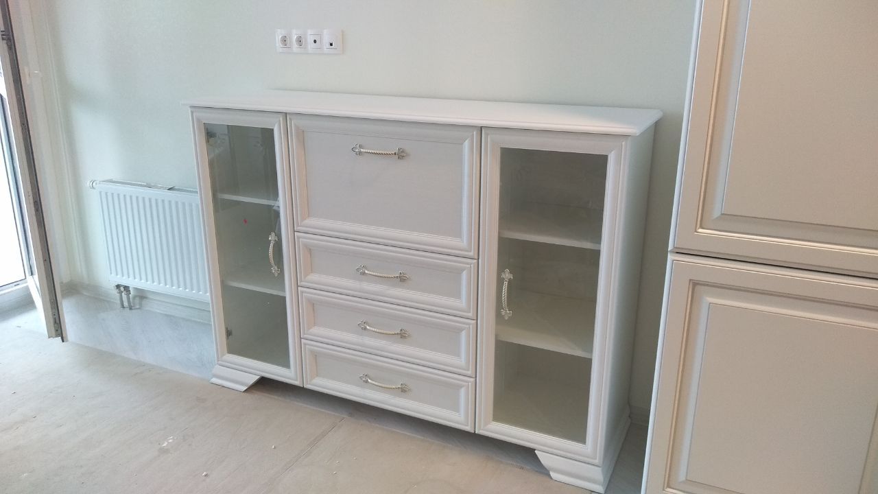 White wooden credenza with glass doors and central drawers against a light wall.