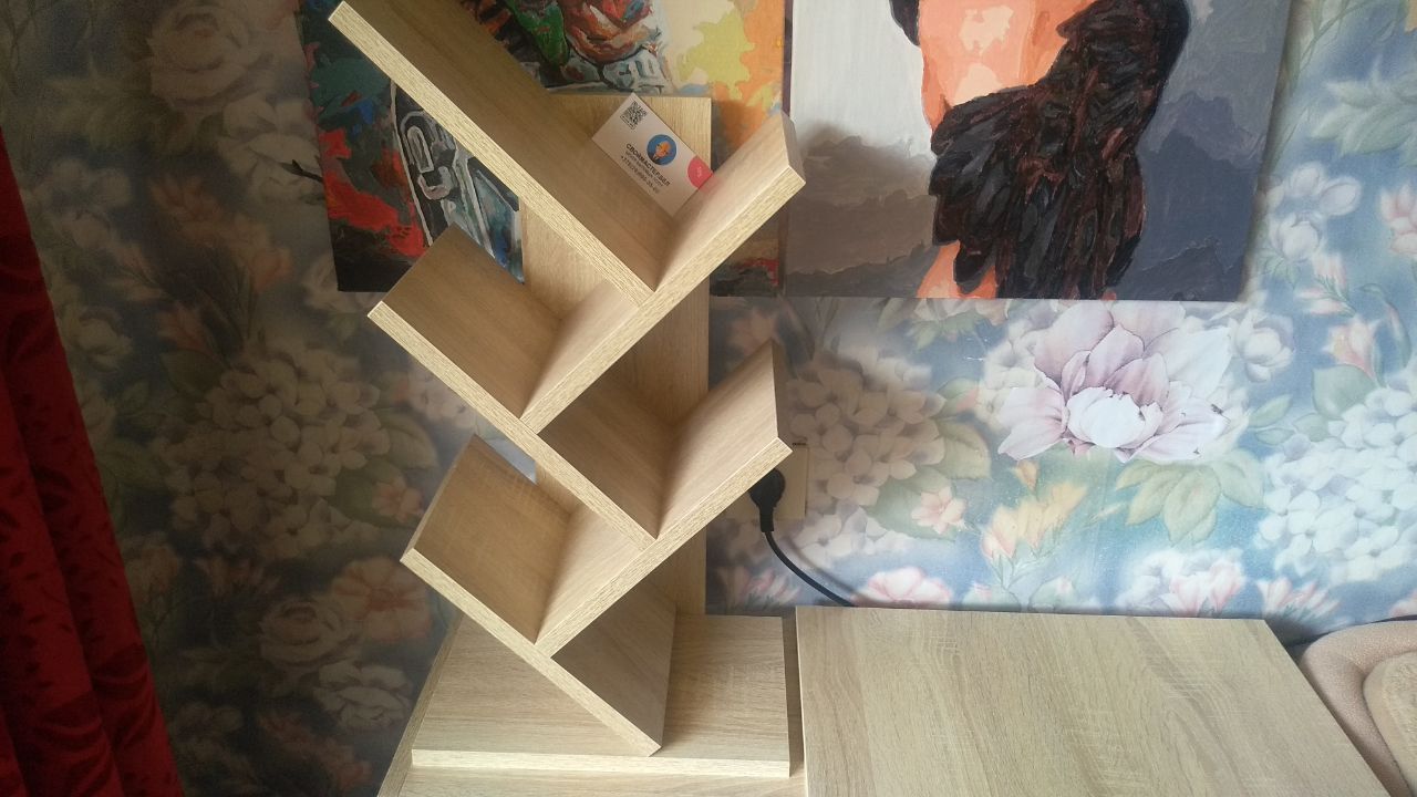 Light wooden zig-zag bookshelf with multiple empty shelves against a patterned wall.
