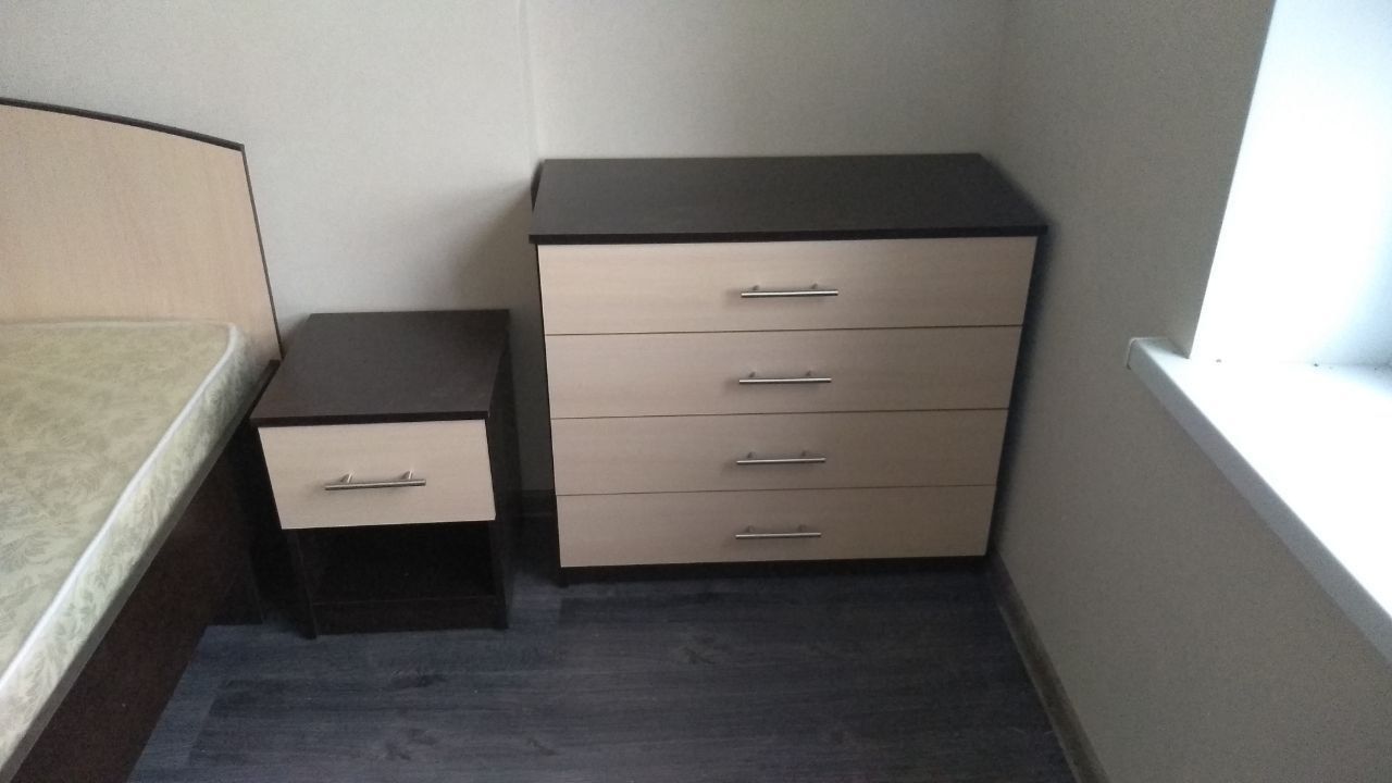 Bedroom corner with dark and light wood bedside table and a four-drawer dresser.