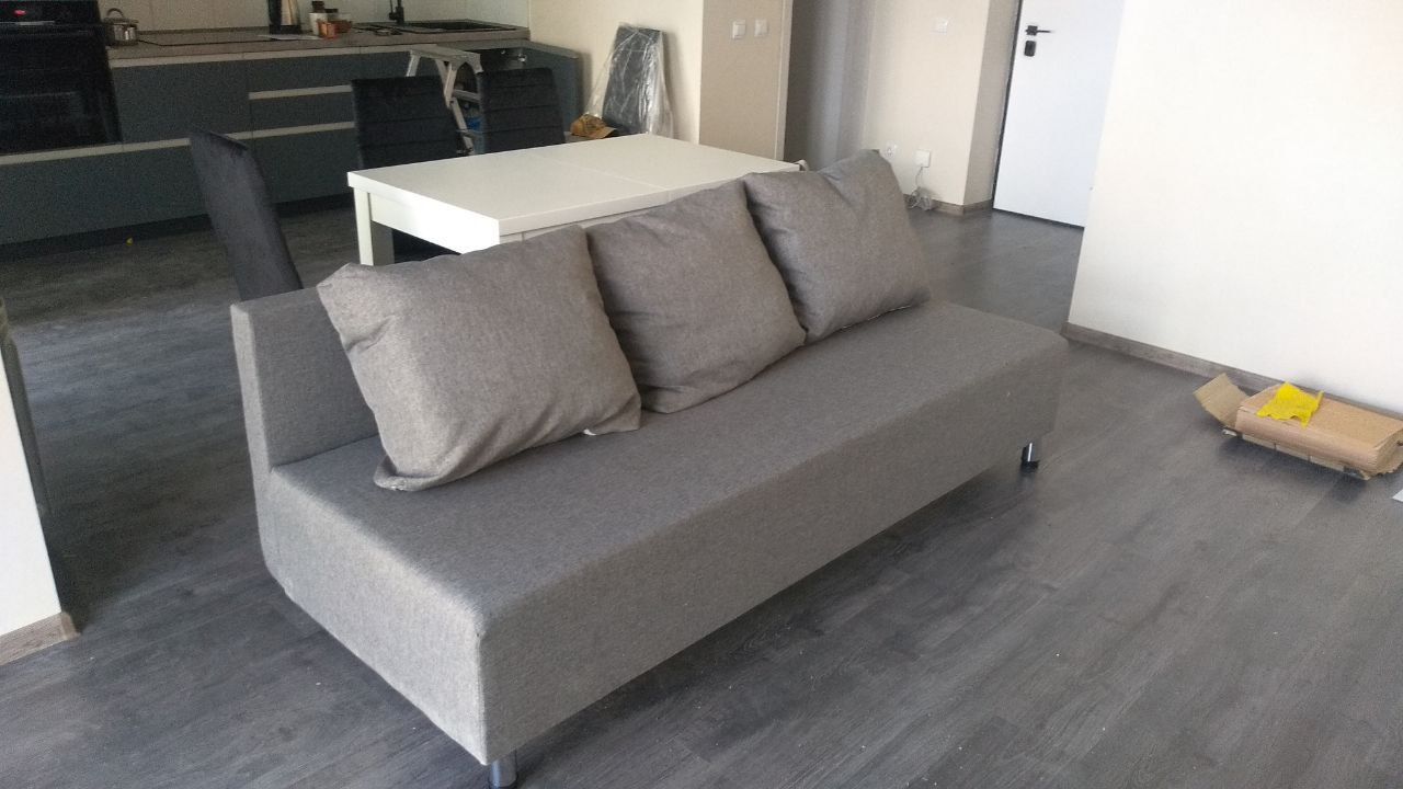Modern grey sofa with three cushions on a dark wood floor.