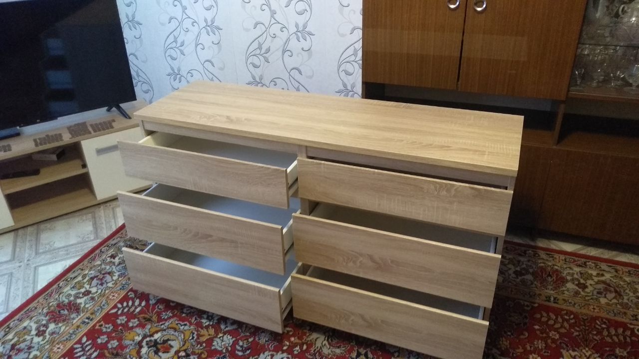 Light wooden dresser with six open, empty drawers positioned on a red patterned rug.